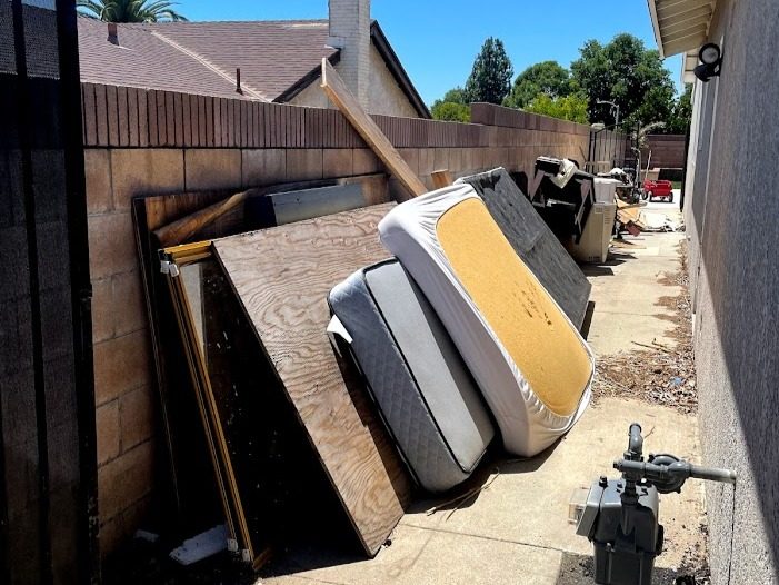 Mattresses, plywood, and household debris piled in a side yard